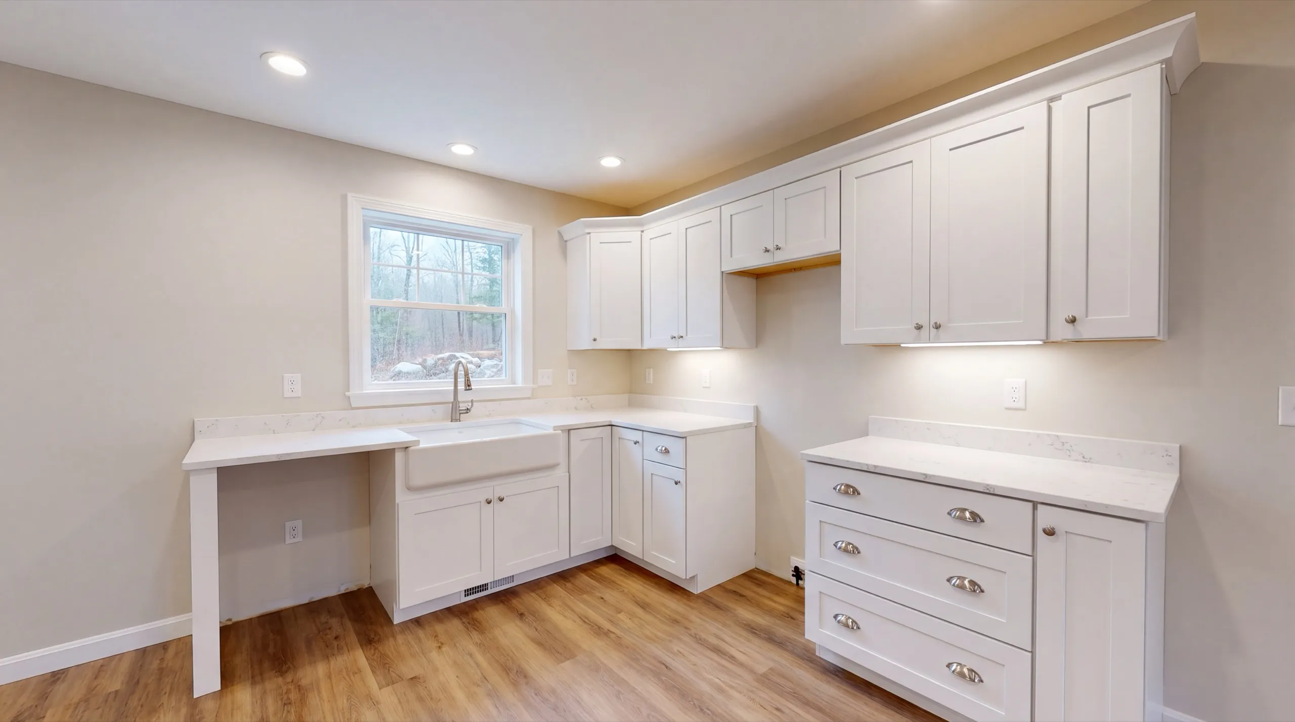 ADU builder Farmingdale Maine: white L-shaped kitchenette with a farmhouse sink and a small desk counter