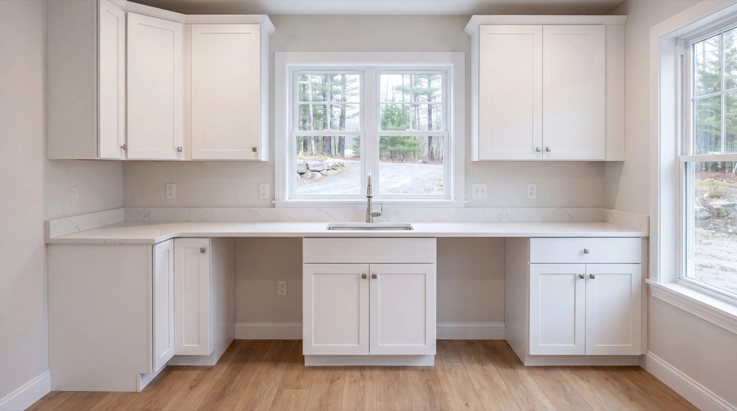 ADU builder West Gardiner Maine: finished wall of white cabinets with a sink under a double window