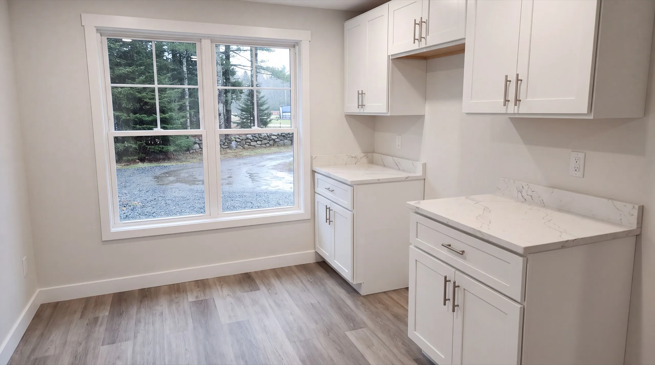 ADU builder Windsor Maine: finished corner kitchen with white cabinets and stone counters by a double window
