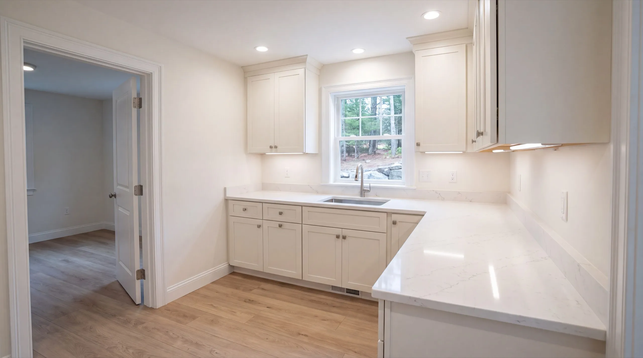 ADU builder Winthrop Maine: finished L-shaped kitchen with white cabinets beside an open bedroom door