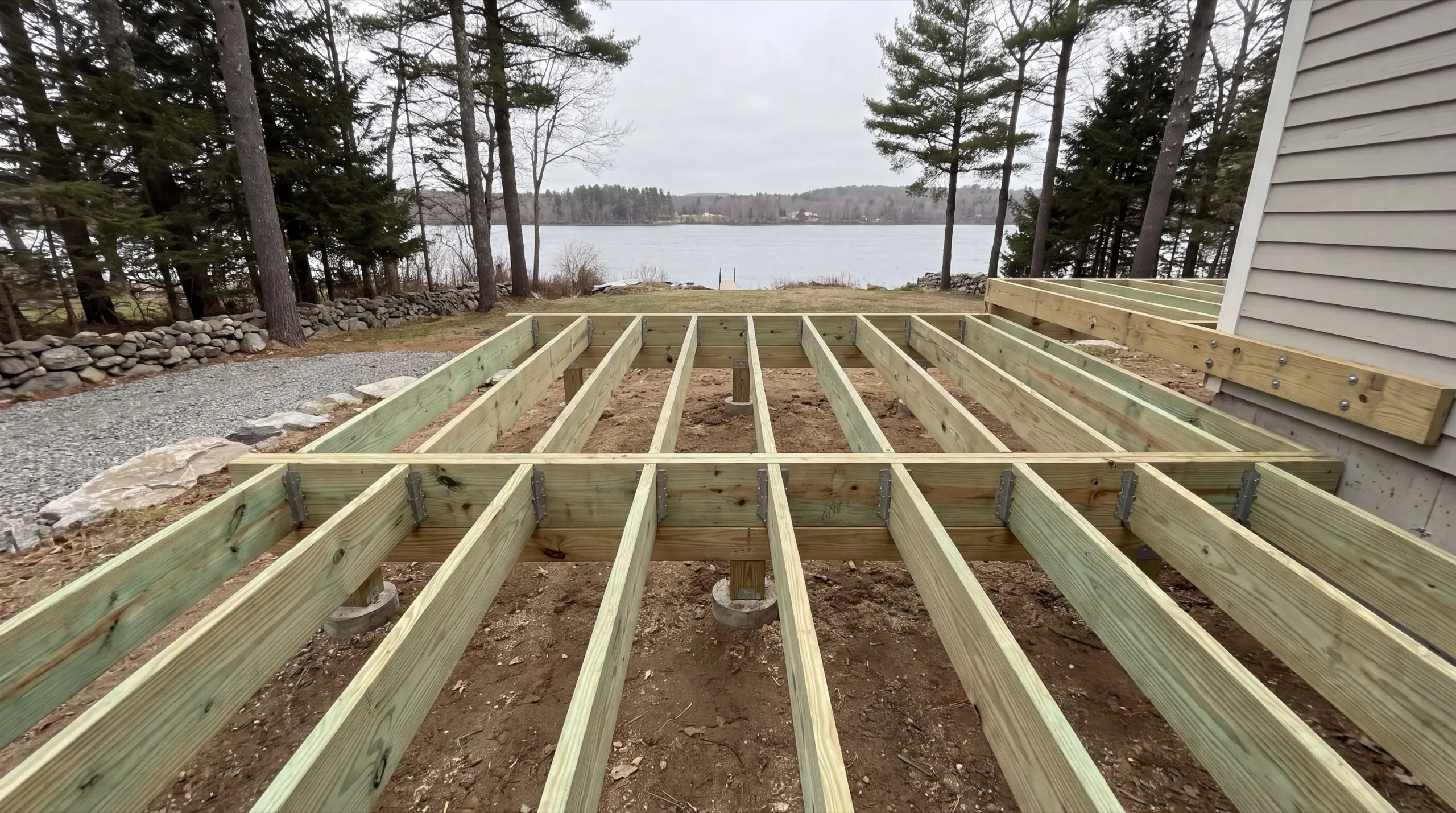 Deck builder Augusta Maine: new pressure-treated deck joists framed on footings beside a house near the water
