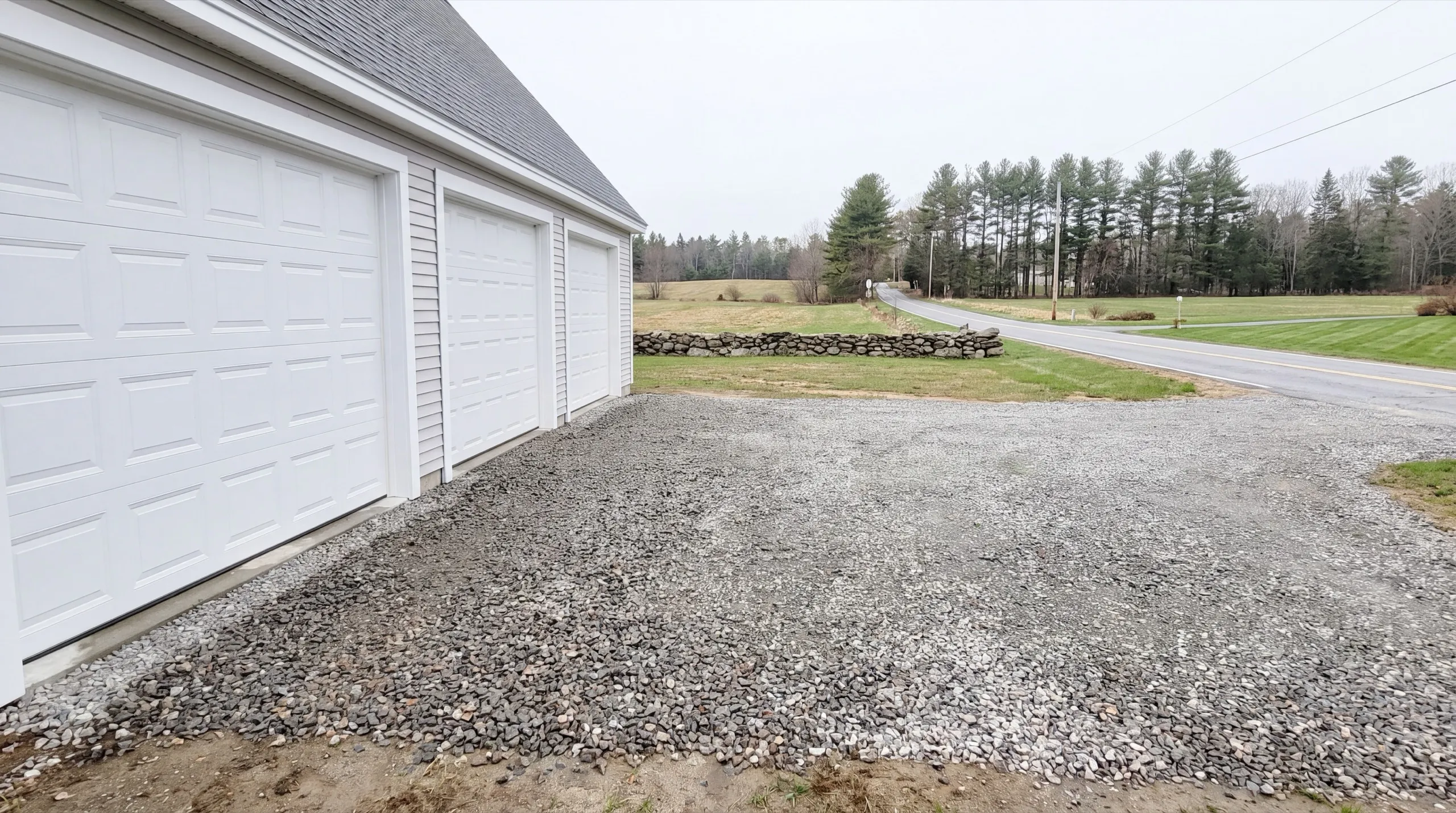 Garage builders Windsor Maine: wide gravel apron along a row of three white garage doors
