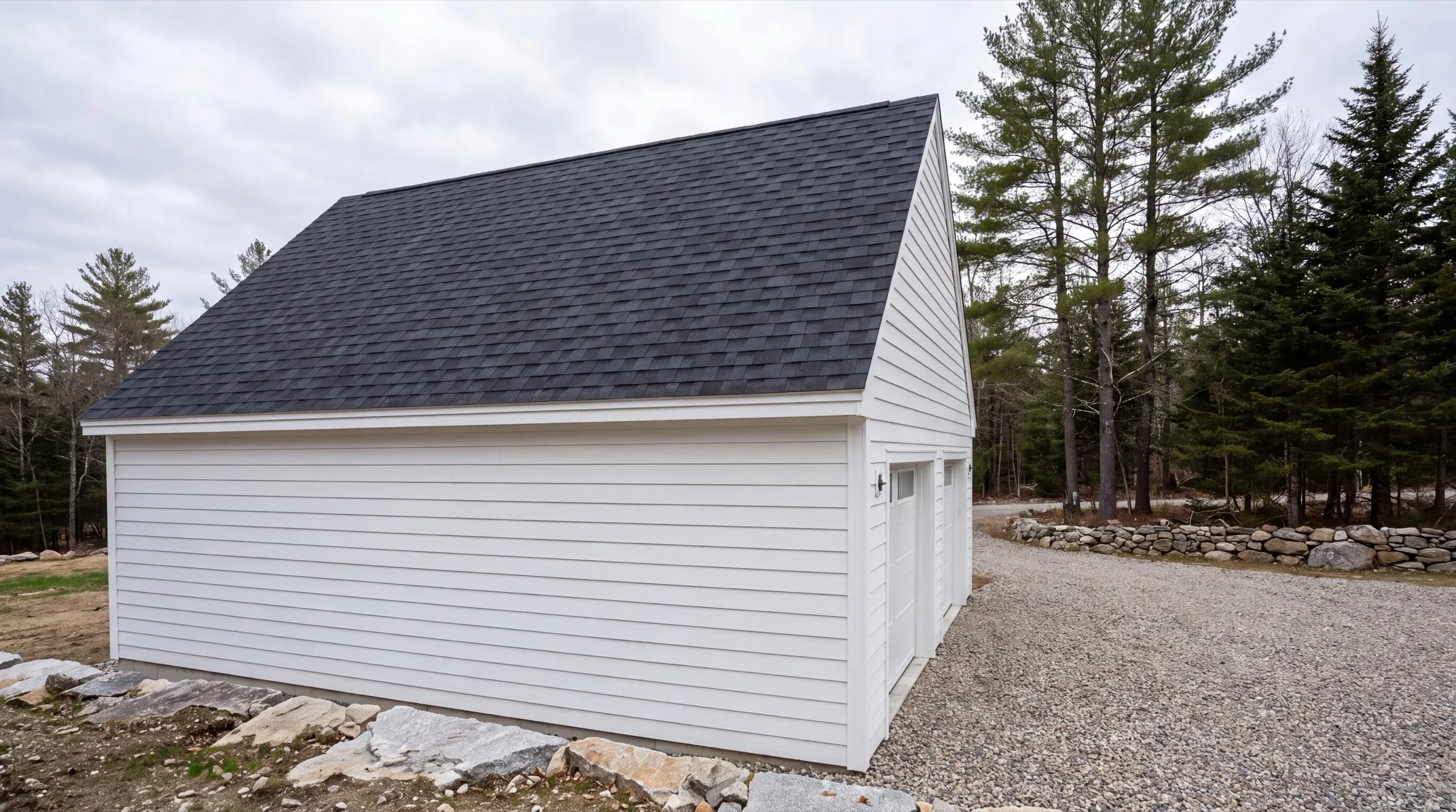 Garage remodeling contractor Randolph Maine: finished white garage with lap siding and a dark roof on a gravel lot