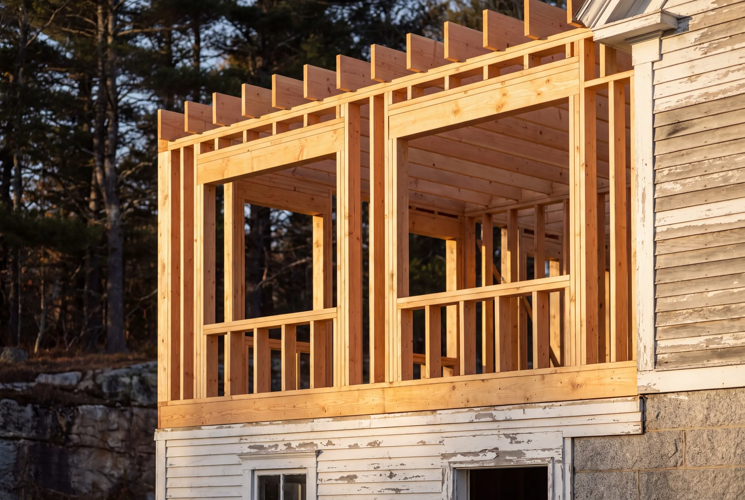 Residential general contractor Wiscasset Maine: new second-story wall framing and joists set on an older white clapboard house