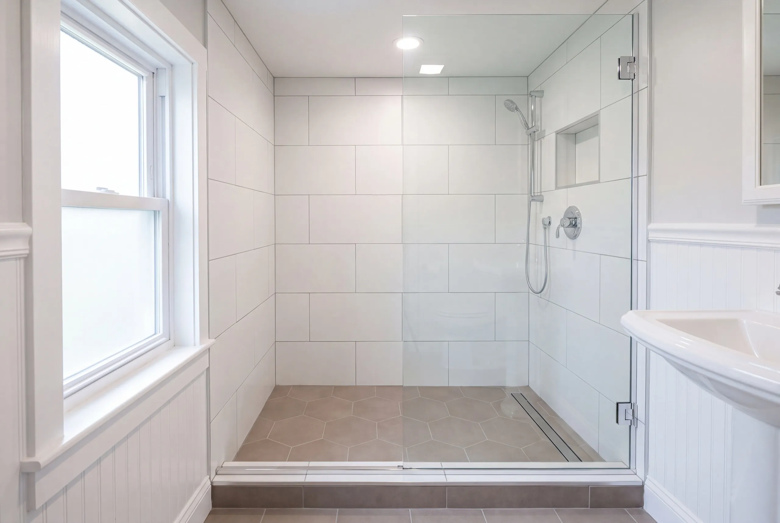 Home renovation contractor Augusta Maine: tiled walk-in shower with a glass door, hex tile floor and a window