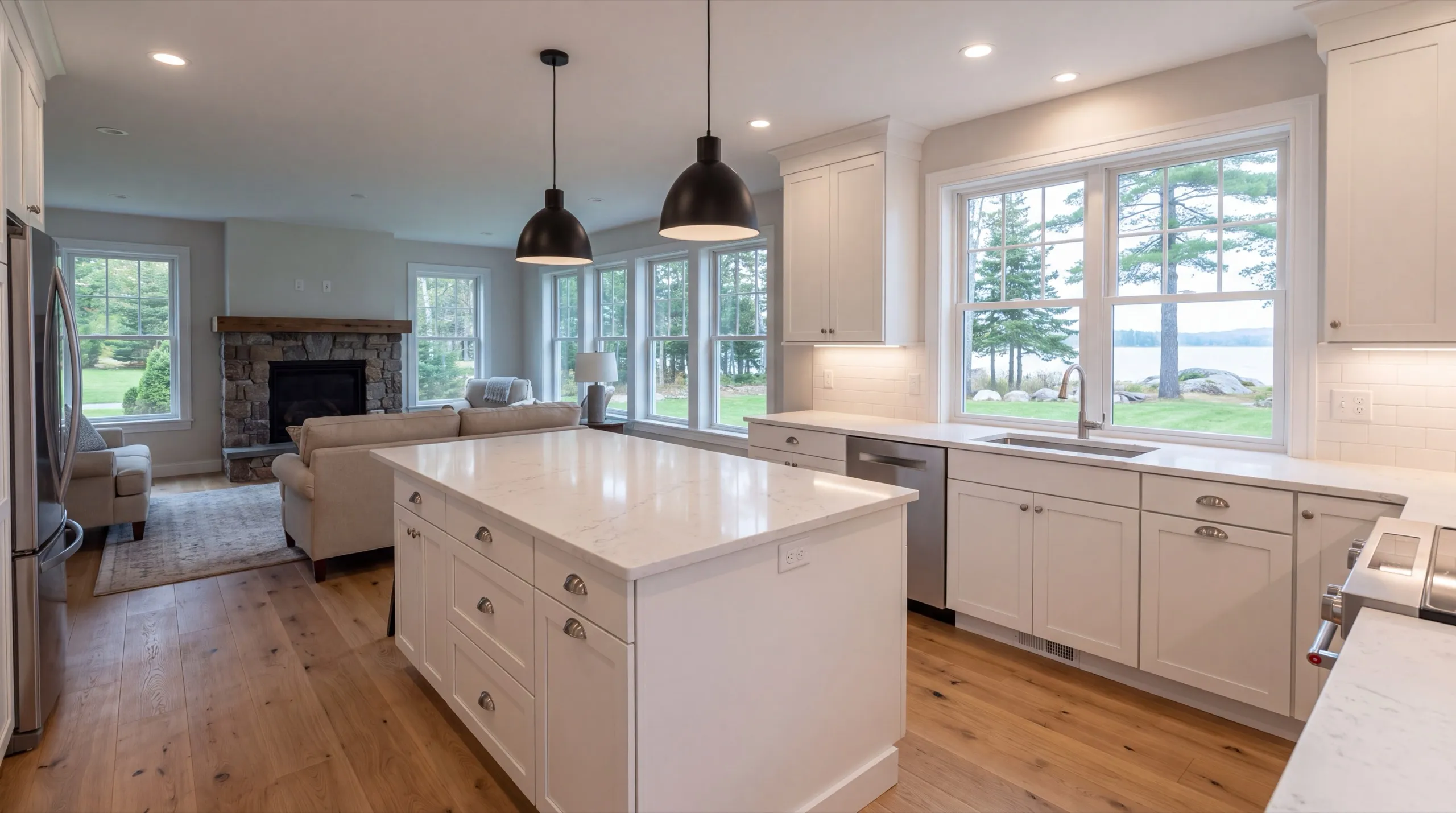 Remodeling in Jefferson, ME: finished white kitchen with an island open to a living room and lake windows