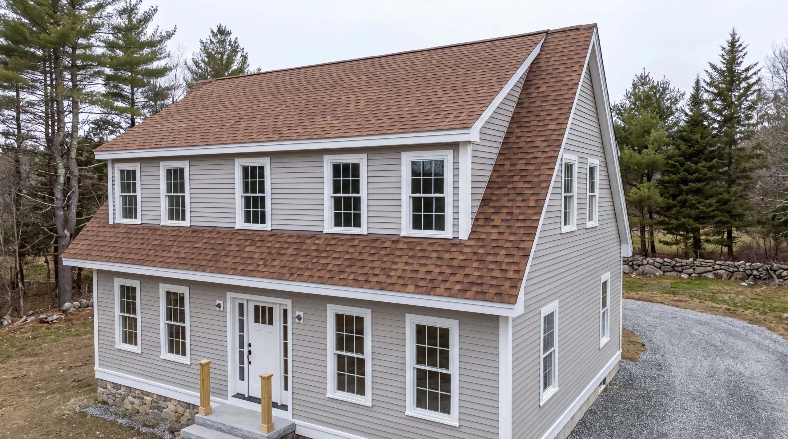 Siding contractor in Wiscasset, ME: finished gray lap-sided cape with a long shed dormer and copper-brown roof